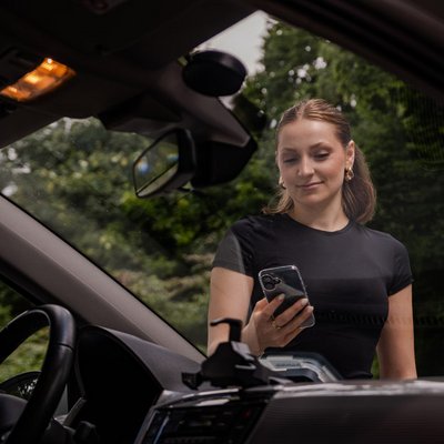 Frau mit Handy durch die Windschutzscheibe des Carsharing-Fahrzeuges