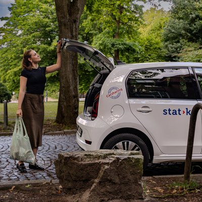 Offener Kofferraum eines Carsharing-Fahrzeuges und eine Frau mit Einkaufstasche