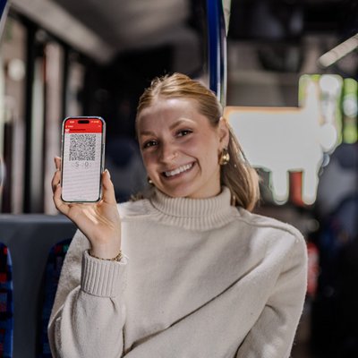 Frau haelt ihr Handy neben sich mit einem Handyticket auf dem Bildschirm