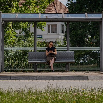 Frau sitzt an einer Bushaltestelle mit ihrem Handy in der Hand