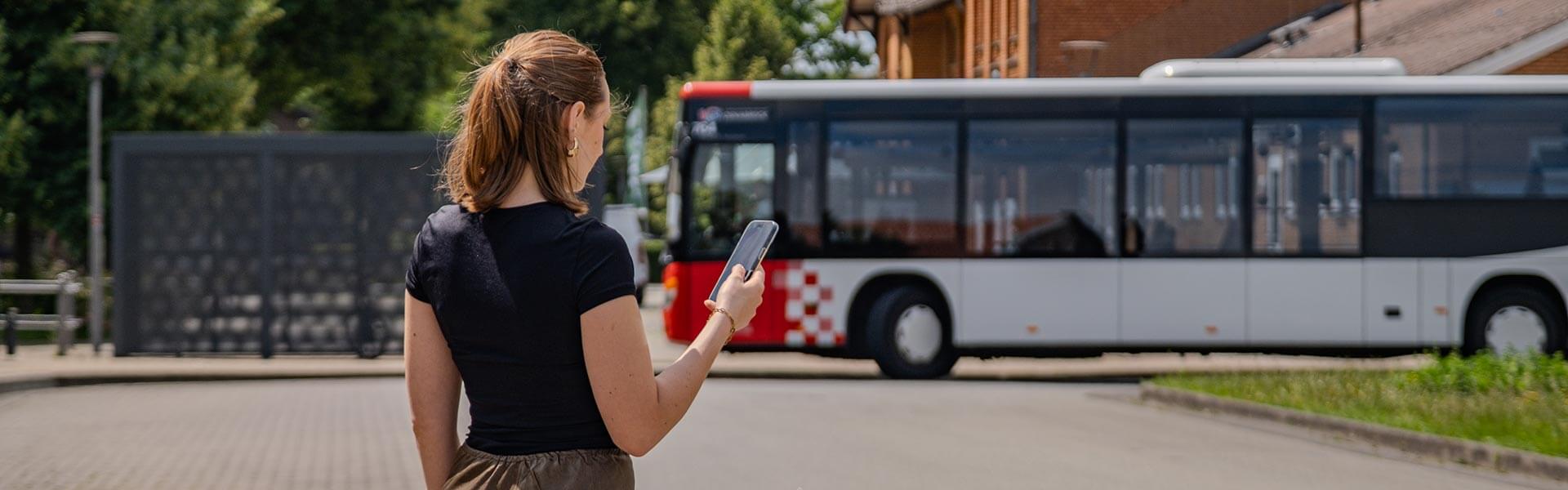 Person mit Smartphone Bus im Hintergrund